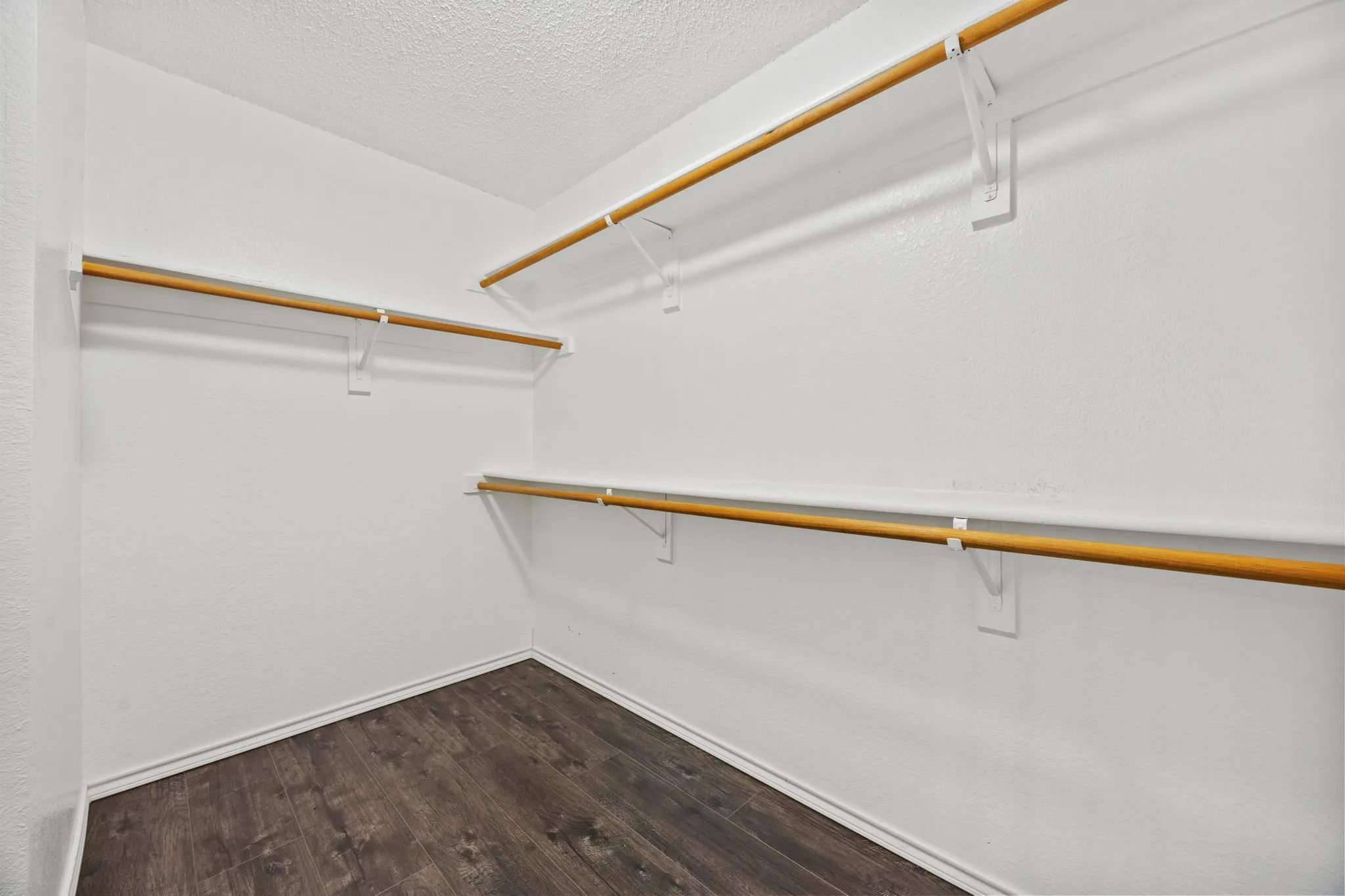 Spacious walk-in closet featuring multiple wood-finish hanging rods with white brackets and dark wood-finish flooring throughout