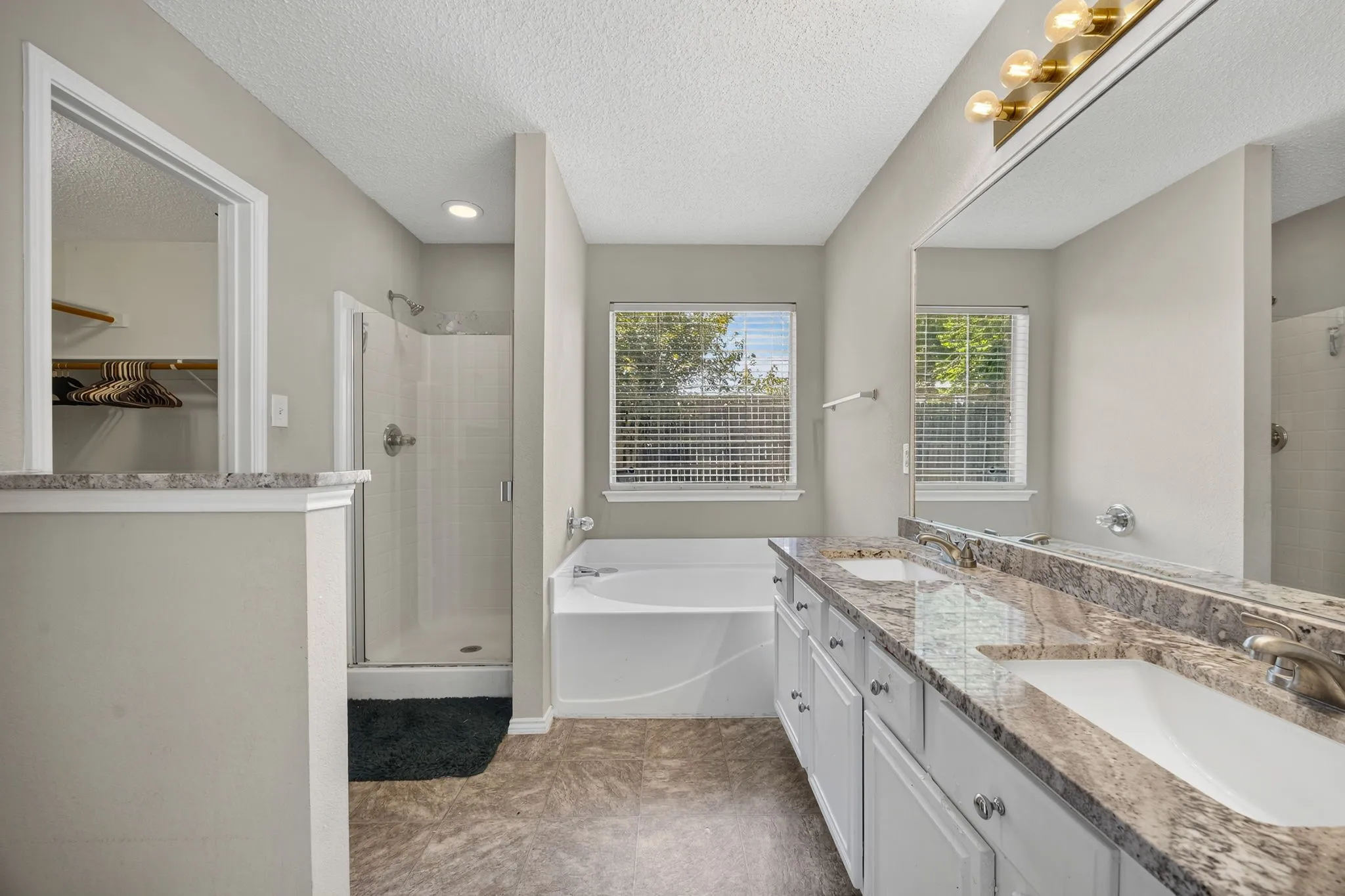 Spa-inspired master bathroom featuring dual vanities with marble-look countertops, white cabinetry, and chrome fixtures