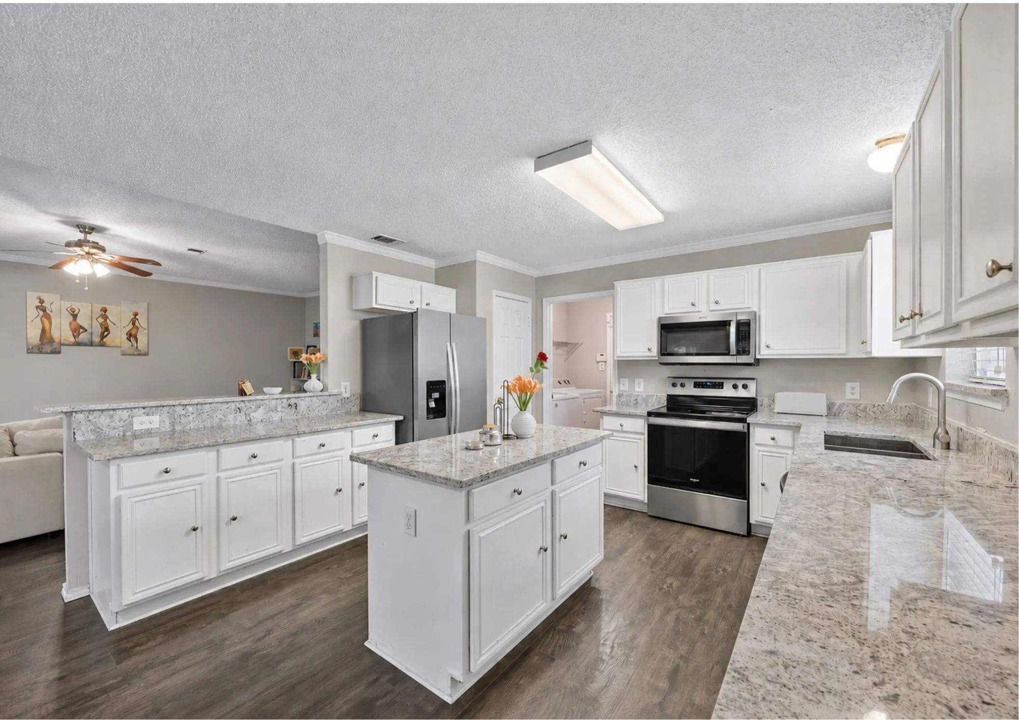 Spacious kitchen featuring white cabinetry, a large center island with granite countertops, stainless steel appliances including a gas range and side-by-side refrigerator, subway tile backsplash, wood-finish flooring, recessed lighting, and abundant counter workspace ideal for meal preparation and entertaining