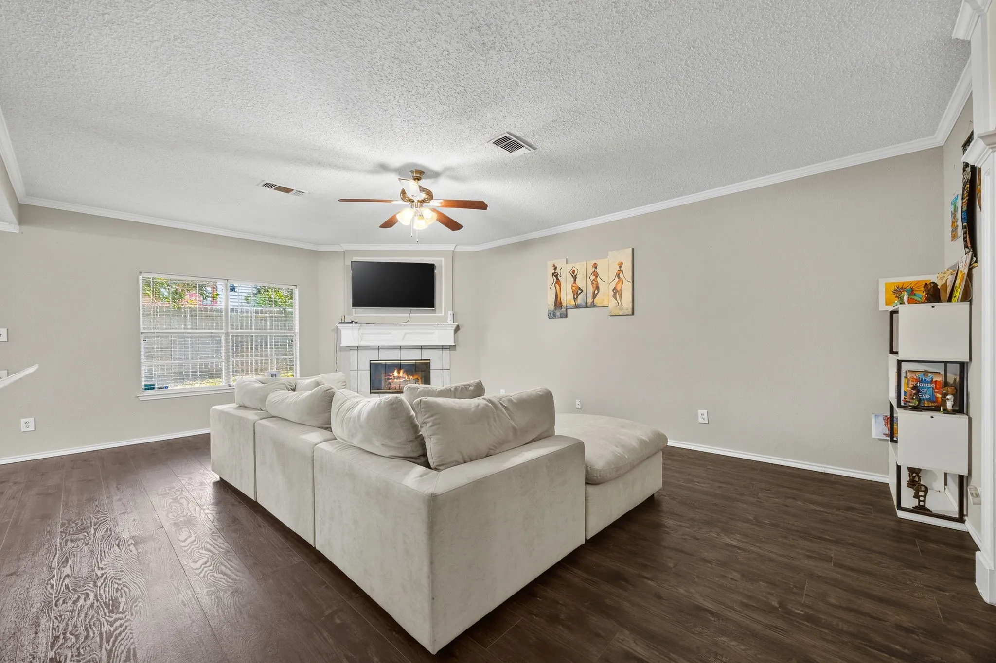 Spacious living room showcasing a wood-finish plank floor, ceiling fan with brushed nickel finish, and a wall-mounted flat-screen television above a fireplace with white surround