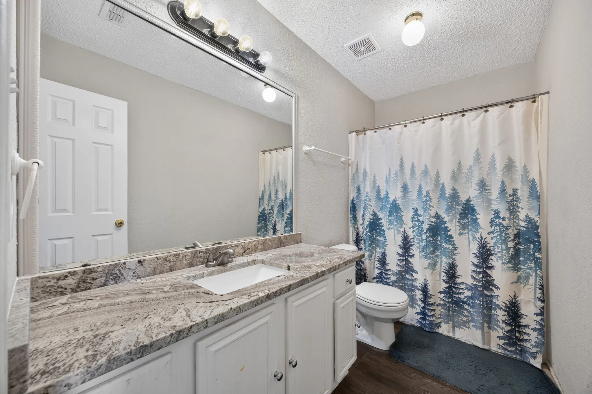 Spa-inspired bathroom featuring a granite-topped vanity with dual sink basins, white cabinetry, and abundant mirror lighting