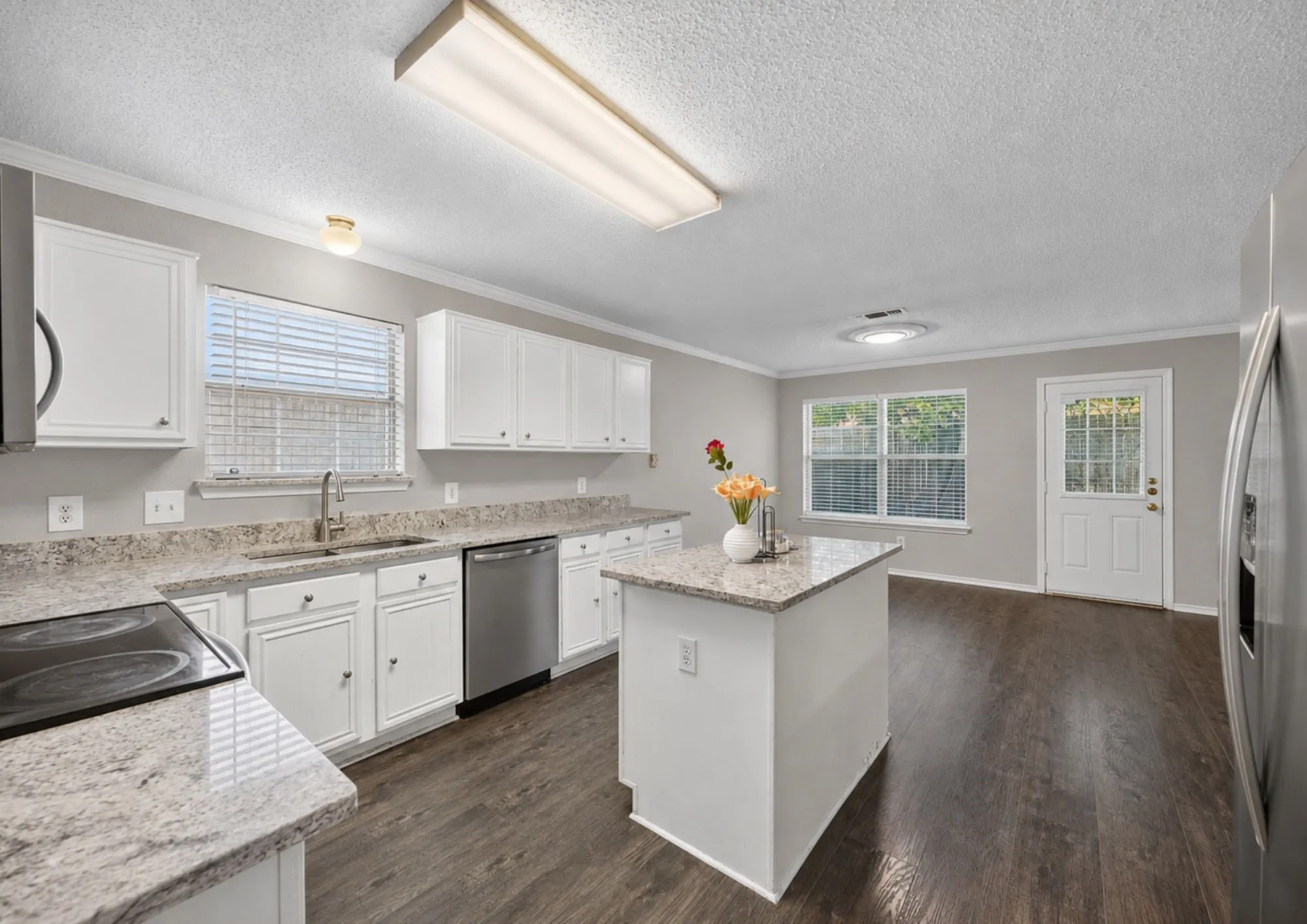 Spacious kitchen featuring white cabinetry, granite countertops, a large center island with additional counter space, stainless steel appliances, and wood-finish flooring throughout
