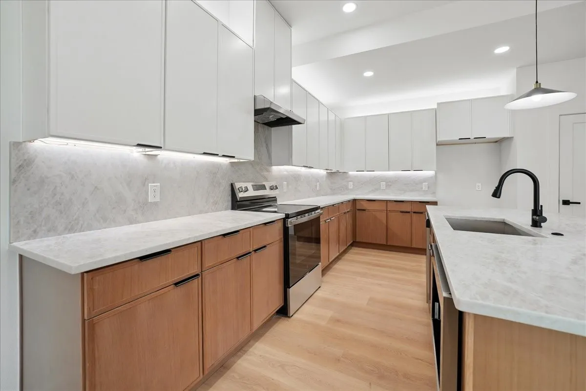 Modern kitchen featuring two-tone cabinetry, light-toned countertops, and a full-height backsplash