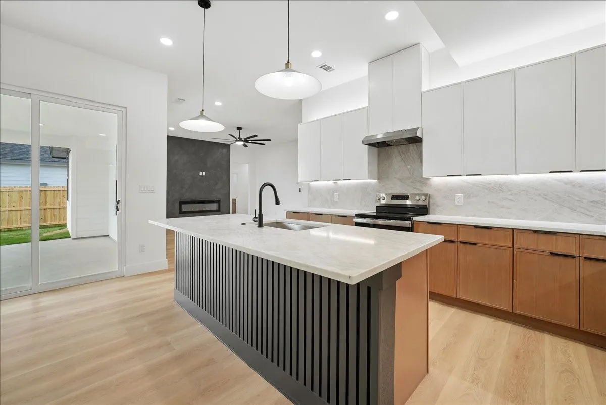 Gourmet kitchen with two-tone cabinetry, a central island featuring a sink and sleek black faucet, and light wood-finish flooring