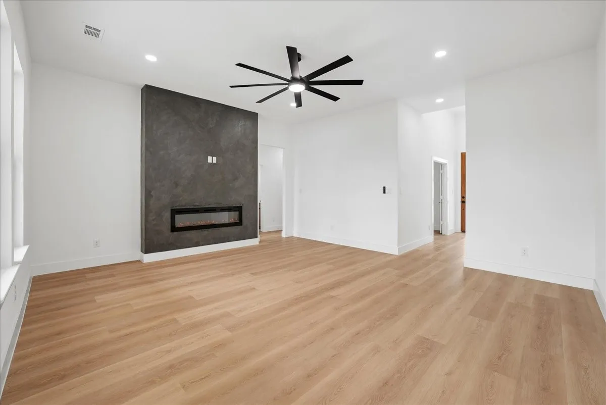 Wood-finish flooring, recessed lighting, modern linear fireplace, textured accent wall, and a ceiling fan