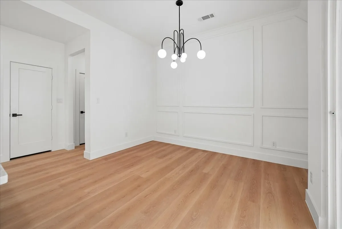 Wood-finish flooring, accent wall with panel molding, modern black chandelier, white flat-panel doors with black hardware, and crisp white baseboards