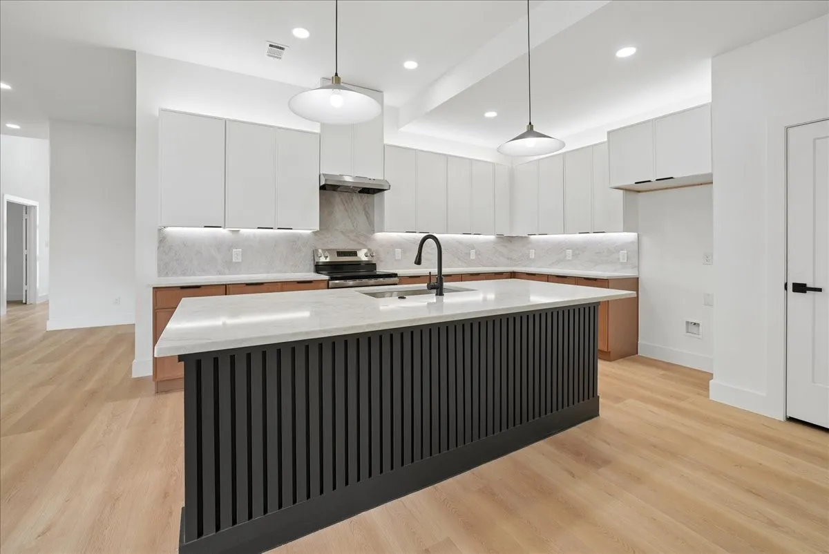 Spacious kitchen featuring a central island with a waterfall countertop, undermount sink, and matte black faucet