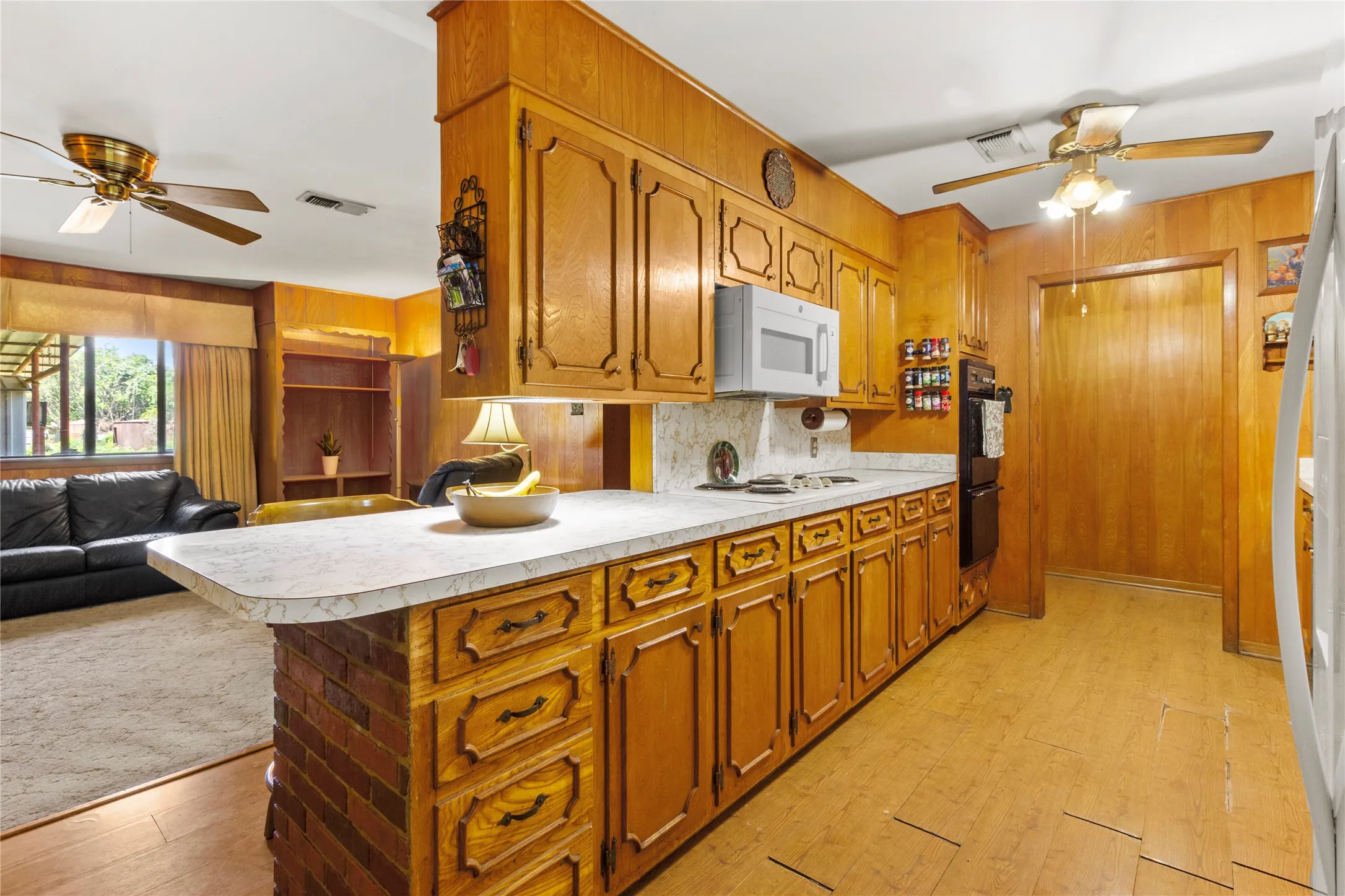 Kitchen featuring ample wood cabinetry, white countertops, built-in microwave, double oven, and wood-paneling accents
