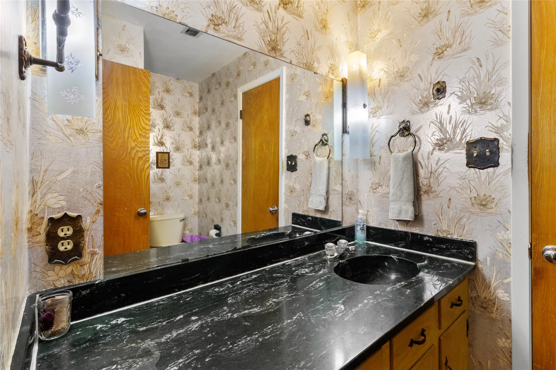 Elegant master bathroom featuring a large framed mirror, black marble-finish double vanity with dual vessel sinks, polished chrome fixtures, and brass-trimmed hardware