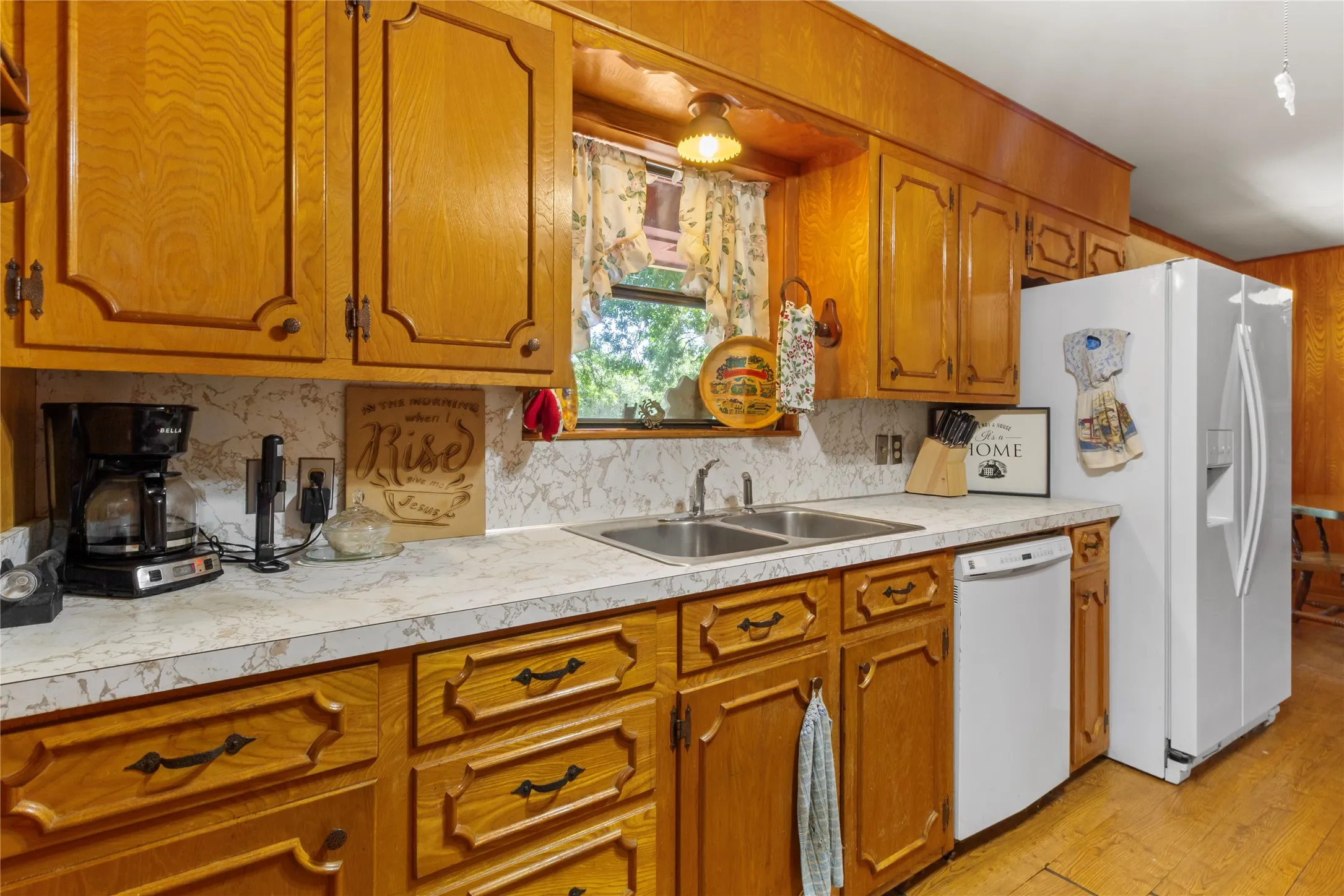 Warm wood cabinetry with decorative hardware frames this functional kitchen, featuring laminate countertops, a stainless steel sink, and white appliances including a refrigerator and range