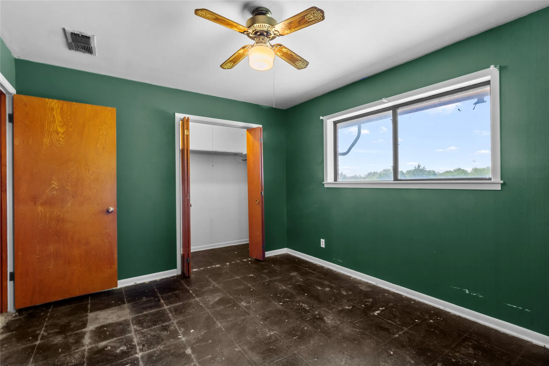 Spacious bedroom featuring rich forest green walls, dark tile flooring, and abundant natural light from a large corner window