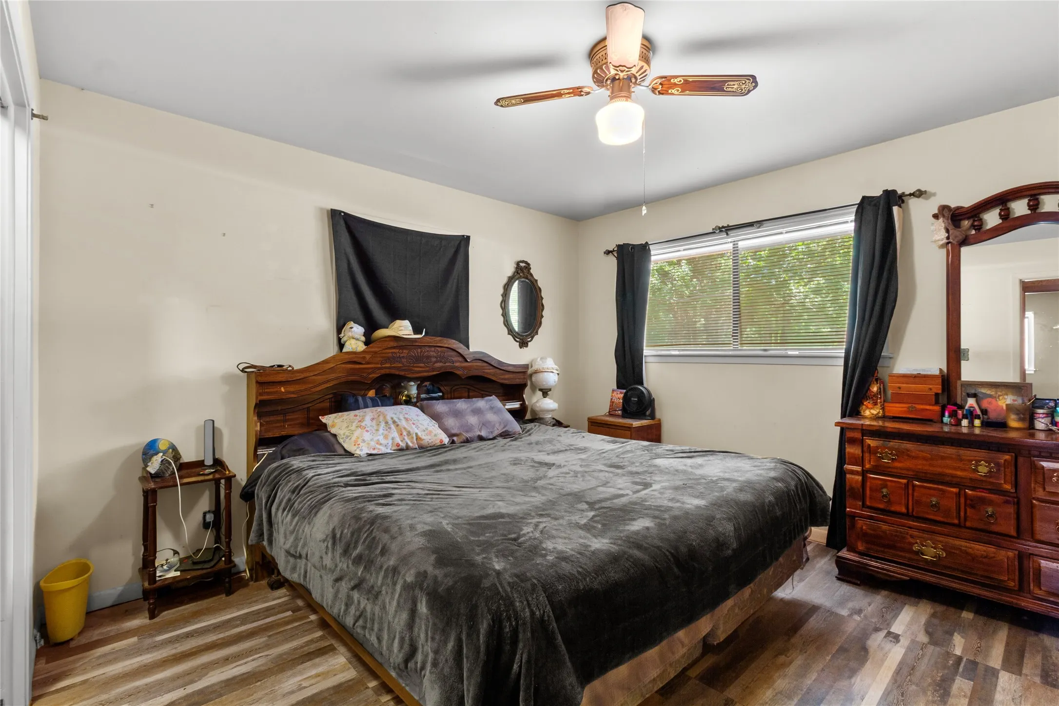 Spacious primary bedroom featuring an ornate wood-finish headboard, wood-finish dresser with mirror, ceiling fan with integrated lighting, and wood-finish flooring throughout