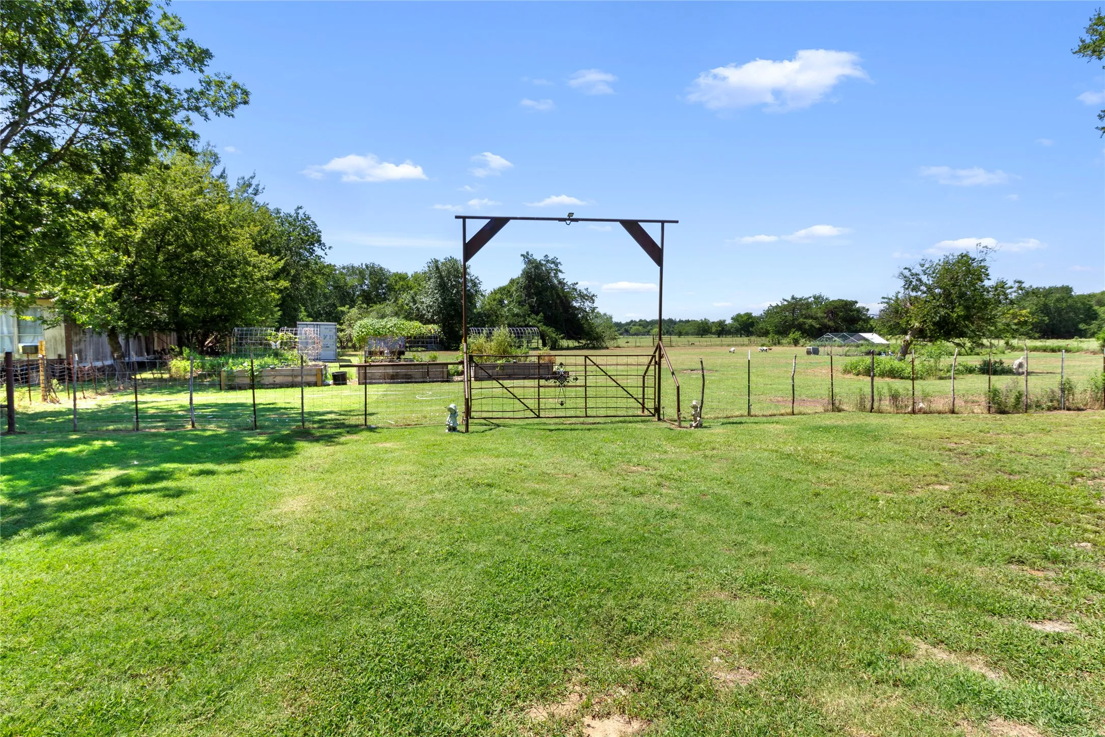 Expansive green lawn with a rustic metal gate, perimeter fencing, and mature trees