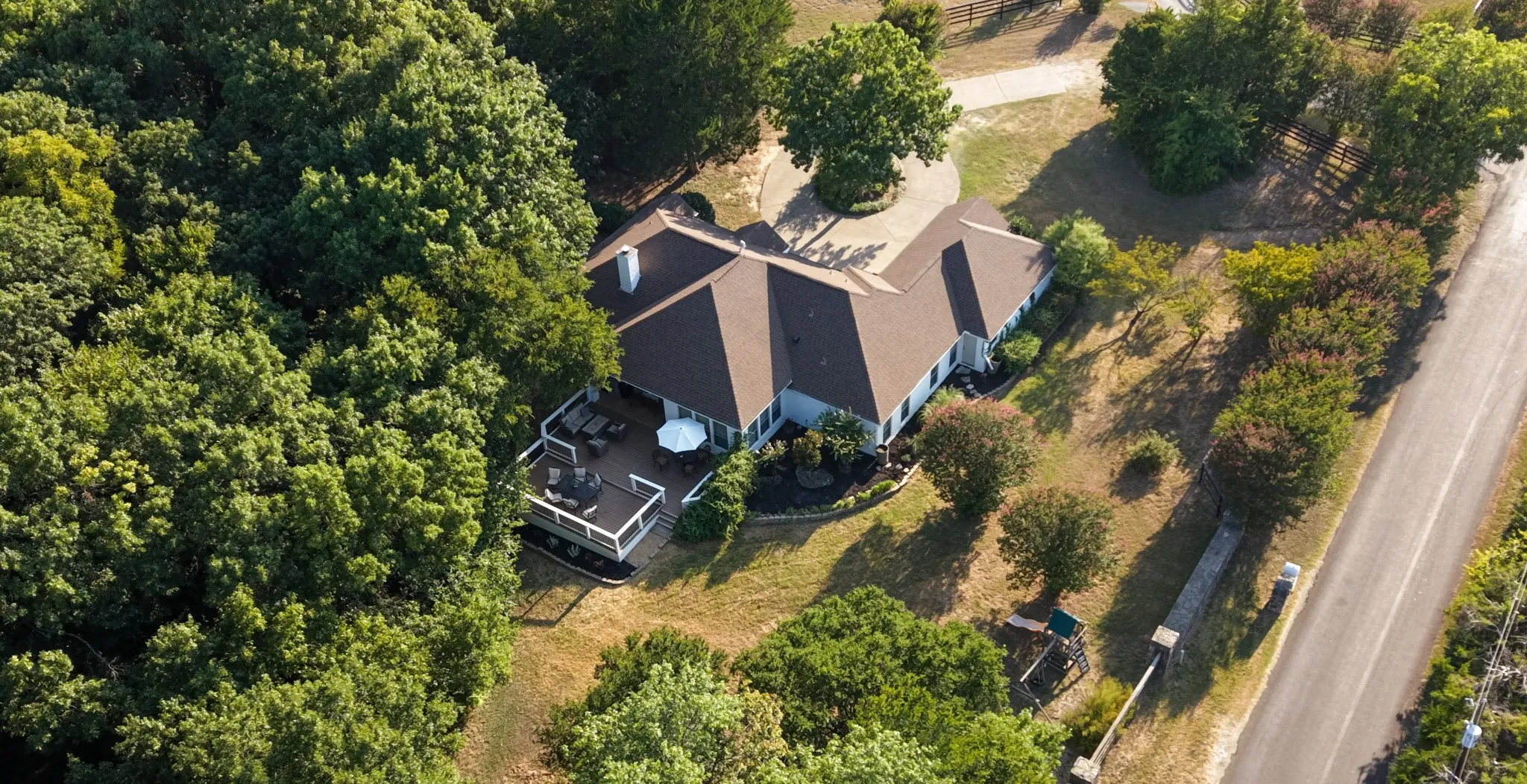 Charming residential home nestled on a wooded lot, featuring a dark-shingled roof with multiple peaks, brick chimney, and mature tree canopy throughout the property