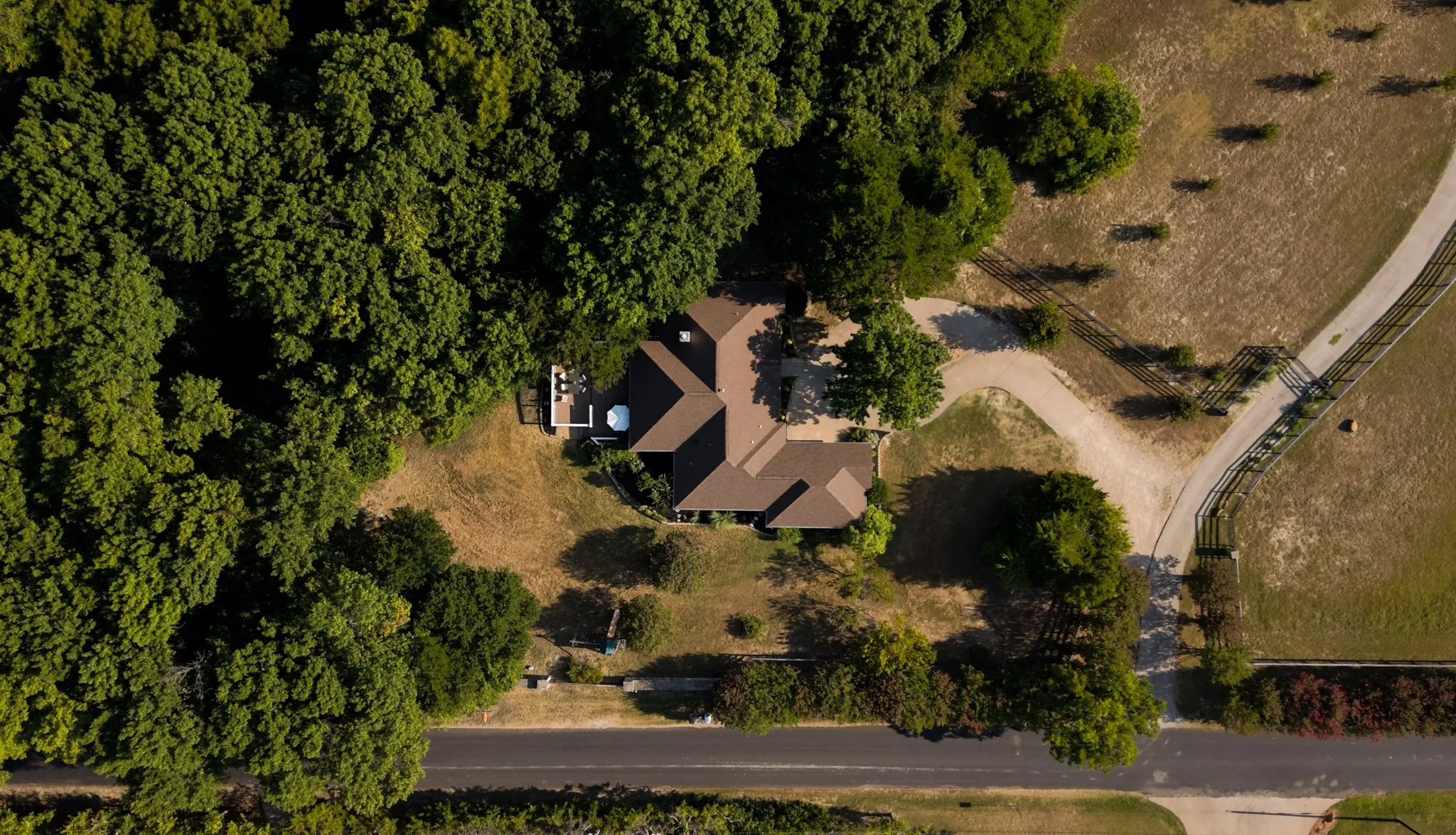 Expansive property featuring a brown-roofed residence nestled amongst mature trees, a private patio, and a dedicated driveway