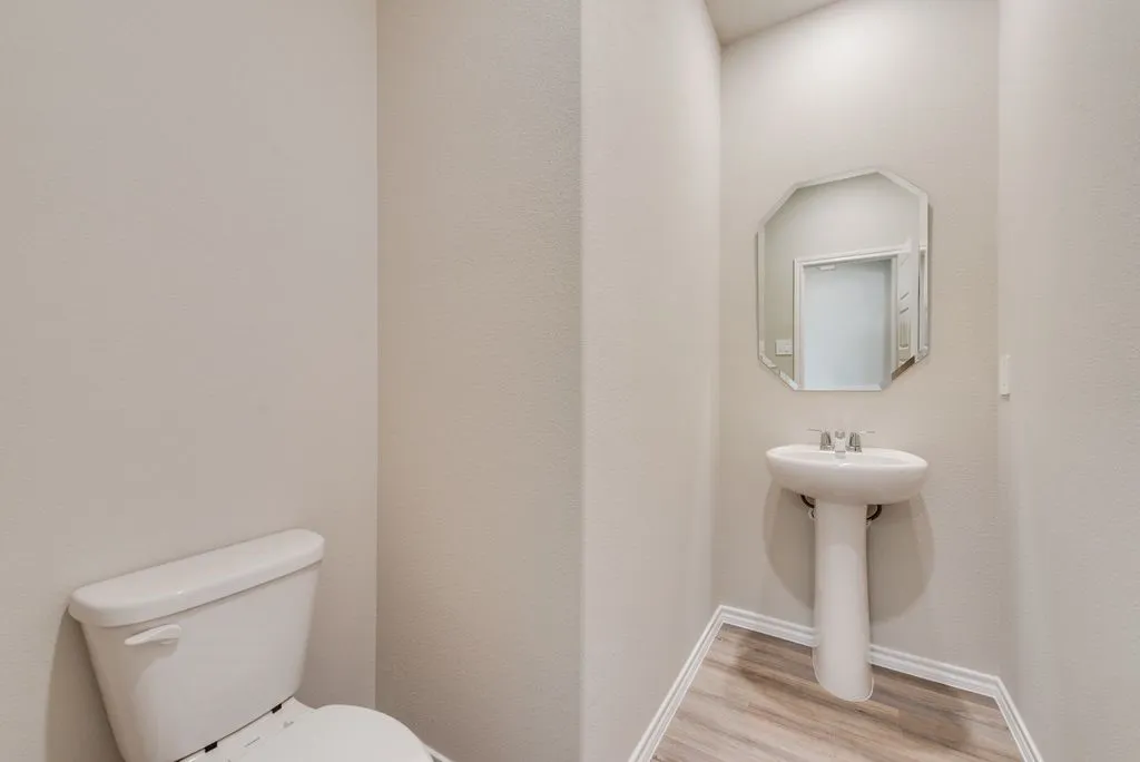 Full bathroom featuring a white pedestal sink, frameless octagonal mirror, and wood-finish flooring