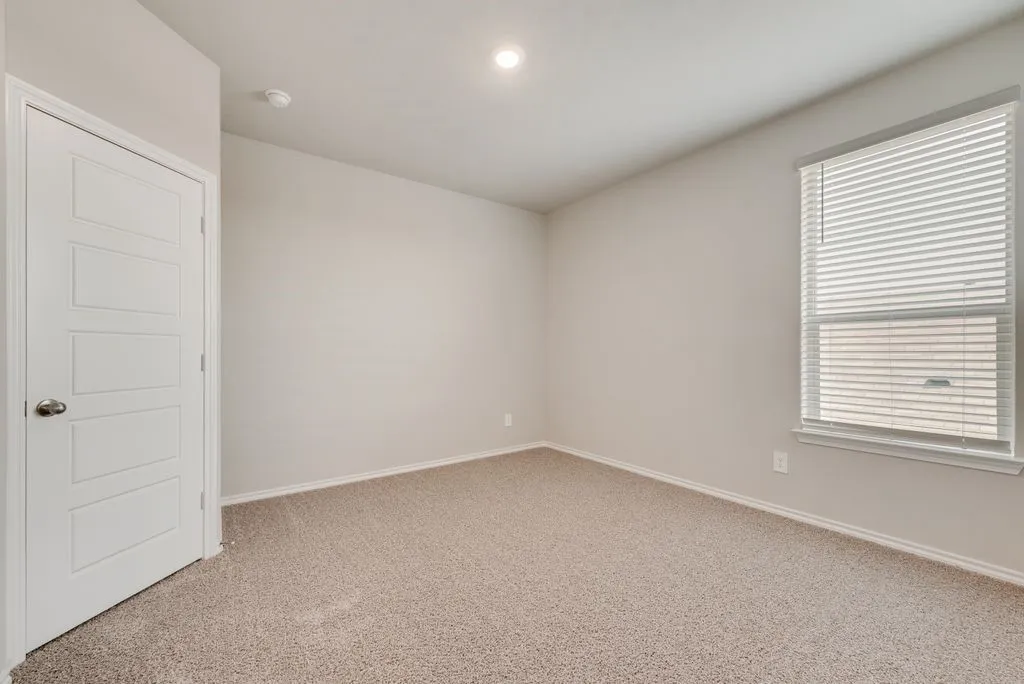 Spacious bedroom featuring neutral walls, recessed ceiling lighting, plush carpet flooring, a large window with plantation shutters providing natural light, and a six-panel white entry door