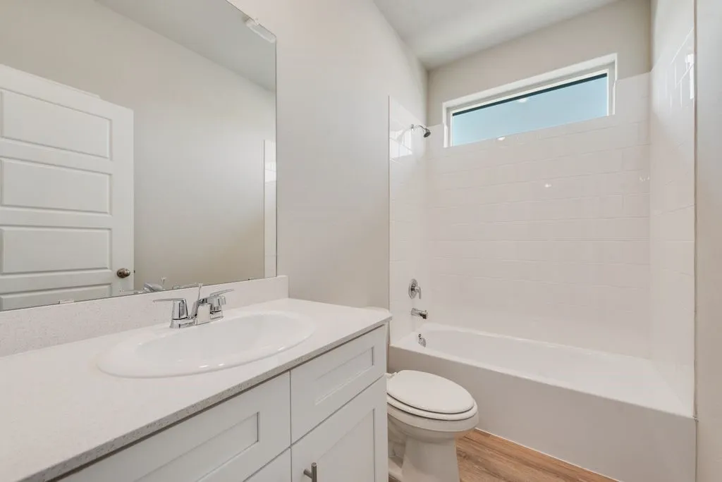 Bright and functional bathroom featuring a white vanity with ample storage, white quartz countertop, chrome faucet, and large mirror with integrated lighting