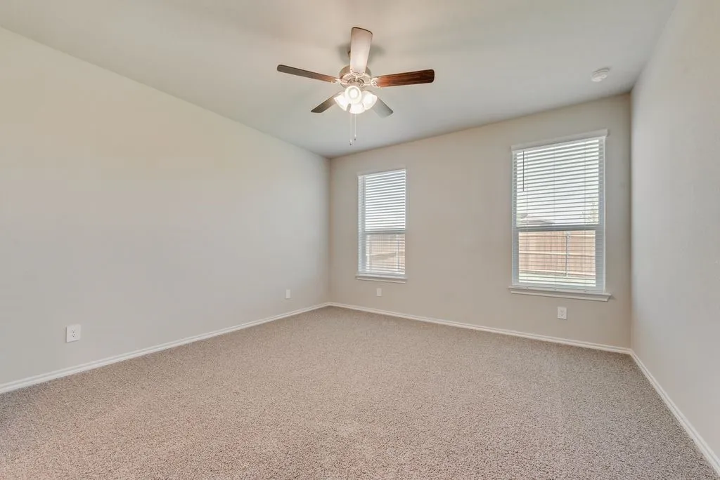 Spacious room featuring neutral carpeting, light-toned walls, and a ceiling fan with integrated lighting