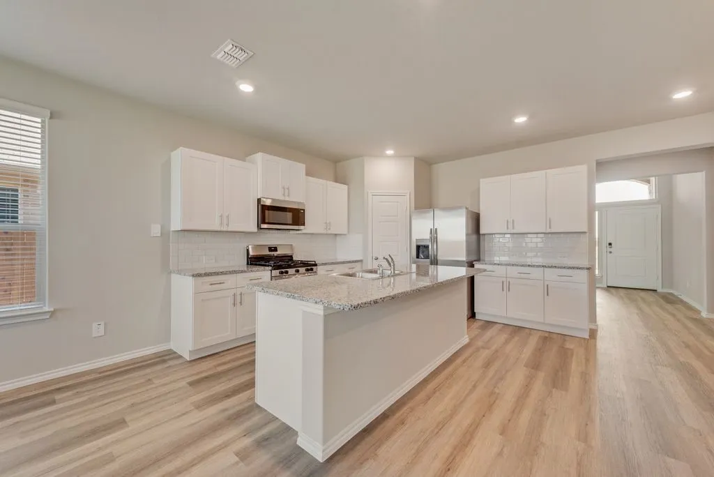 Spacious kitchen featuring white cabinetry, stainless steel appliances, quartz countertops, and a large center island with extended seating