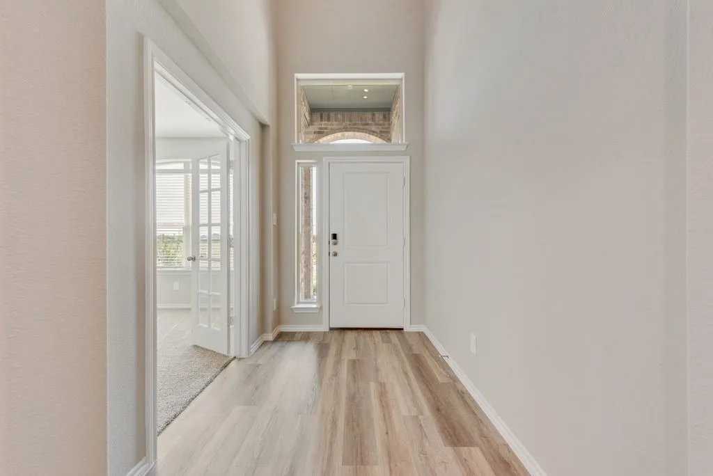 Bright hallway featuring wide-plank wood-finish flooring, clean white walls, and abundant natural light from glass French doors