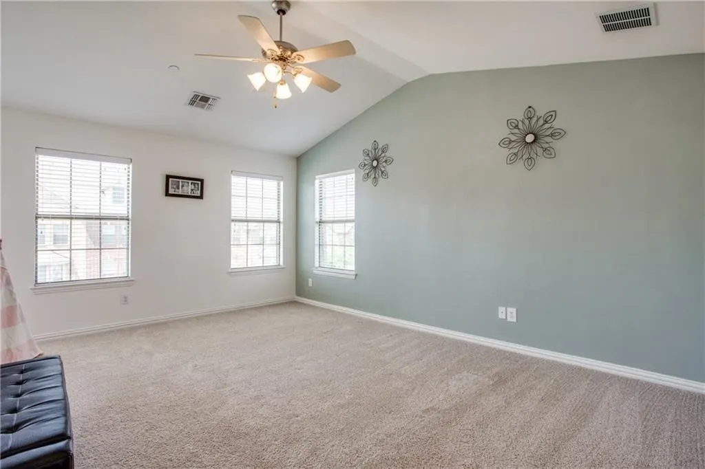 Carpeted spare room featuring plenty of natural light, visible vents, and vaulted ceiling