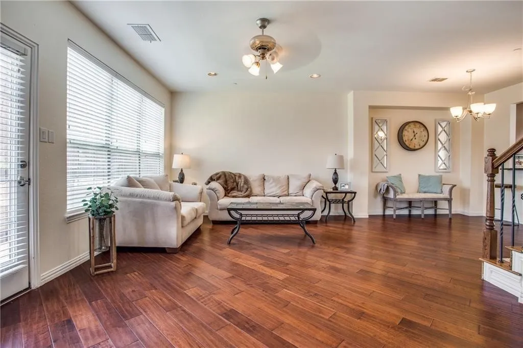 Living area featuring dark wood finished floors, ceiling fan with notable chandelier, baseboards, and visible vents