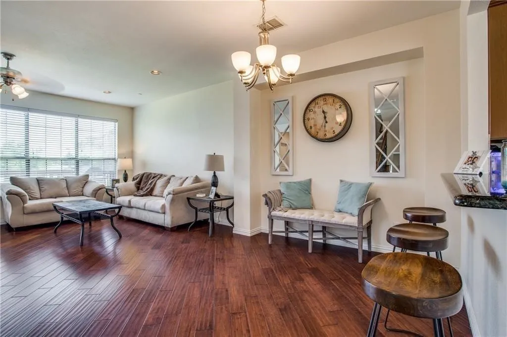 Living area with baseboards, visible vents, ceiling fan with notable chandelier, and dark wood-style flooring