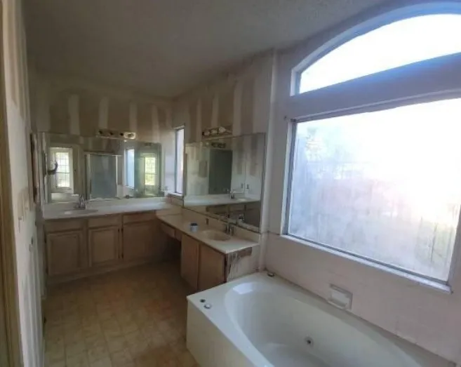 Spacious bathroom featuring a built-in soaking tub with jets, large windows with an arched transom, and dual vanity areas with integrated sinks and mirrored walls