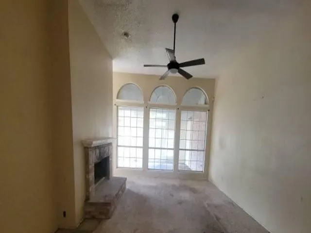 Bright living space featuring three arched transom windows with gridded panes, neutral wall finishes, and a ceiling fan with dark metal blades