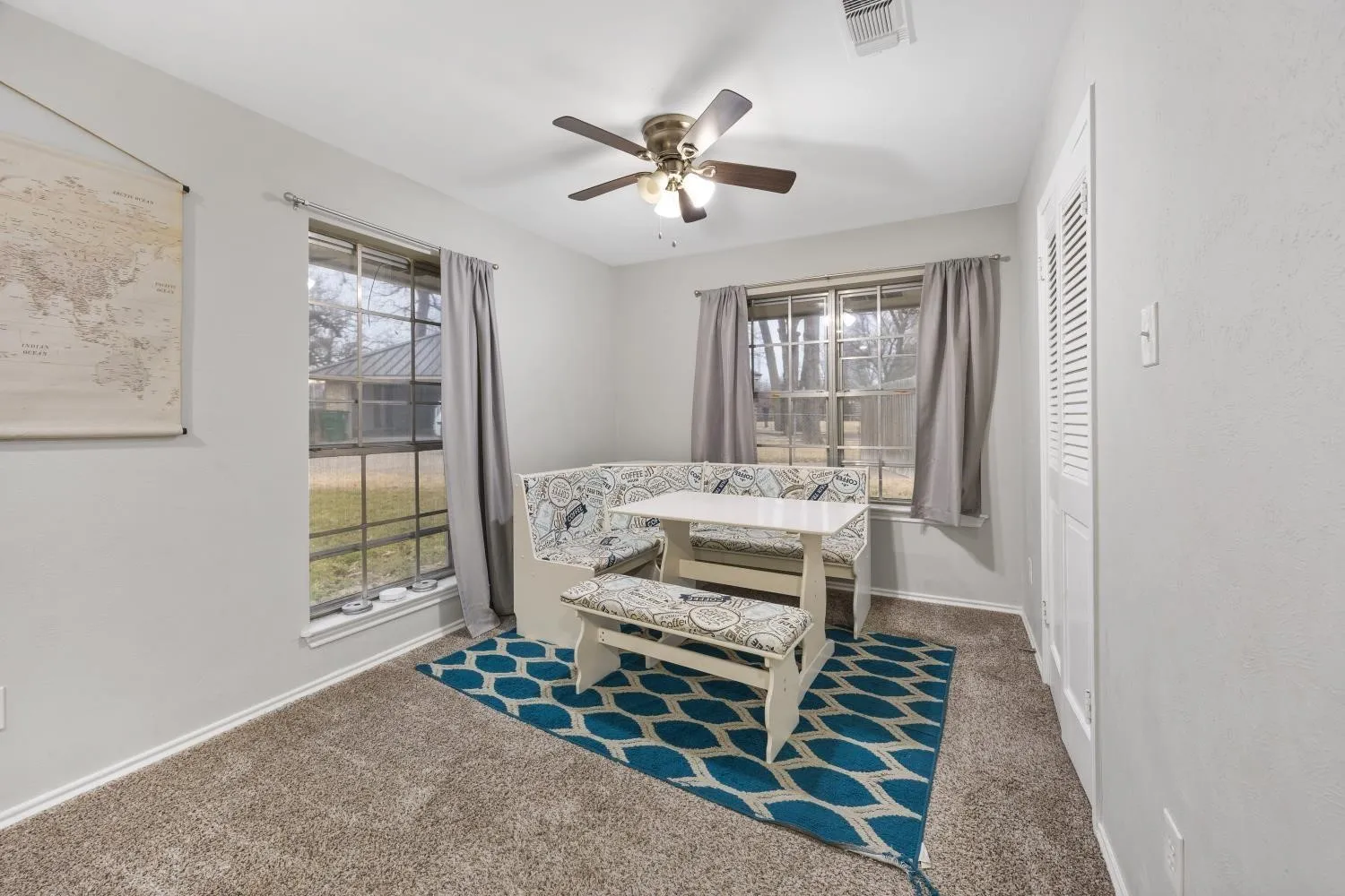 Bright bedroom retreat featuring expansive windows with natural light, ceiling fan with integrated lighting, neutral carpet flooring, and a geometric area rug accent