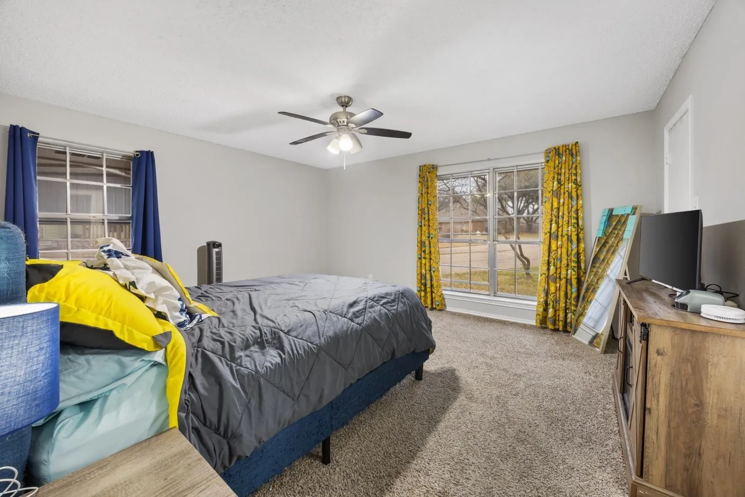 Carpeted room featuring a ceiling fan with light fixture, two windows, and light gray wall paint