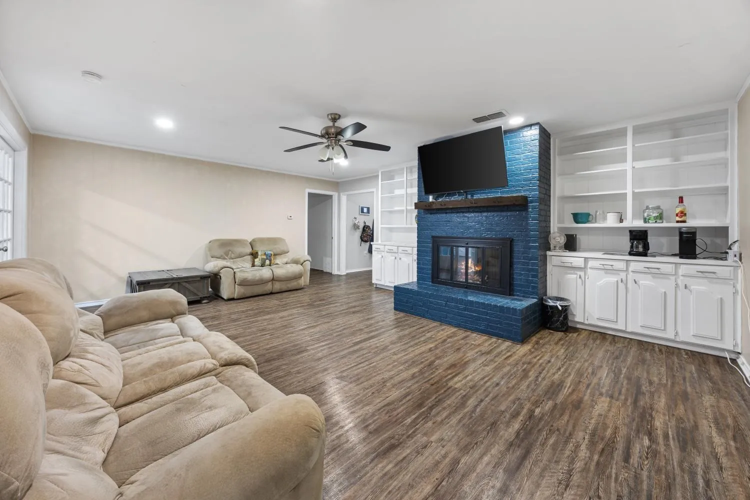 Spacious living area featuring wood-finish flooring, a blue brick fireplace with mounted television, and built-in white cabinetry with shelving