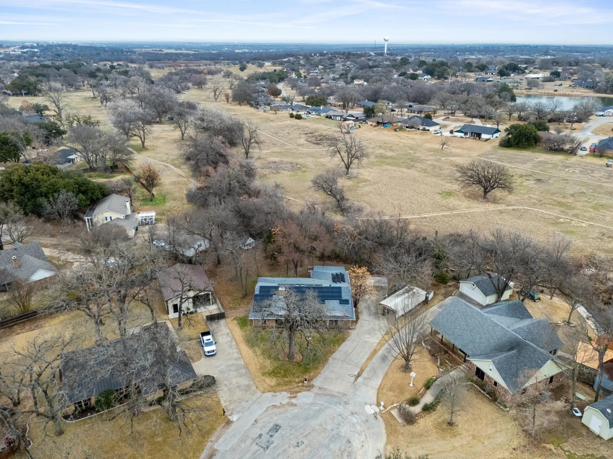 Aerial view showcasing a rural residential property with a modern home featuring a gray roof and stone exterior, situated on expansive acreage