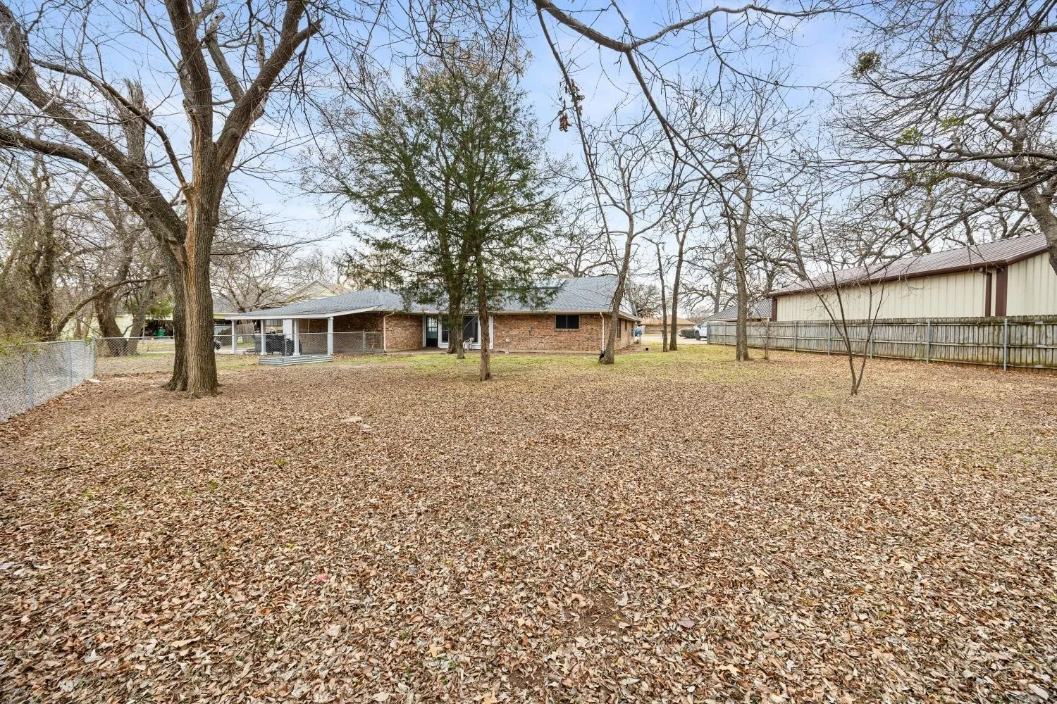 Expansive backyard featuring mature trees and a brick-built residence with a covered patio