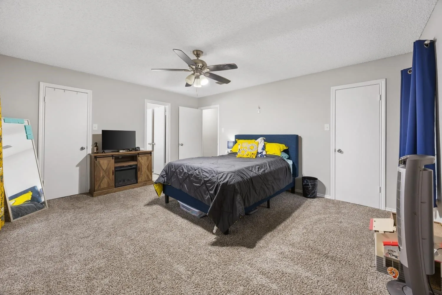 Spacious carpeted room featuring a ceiling fan, light gray walls, and multiple white panel doors