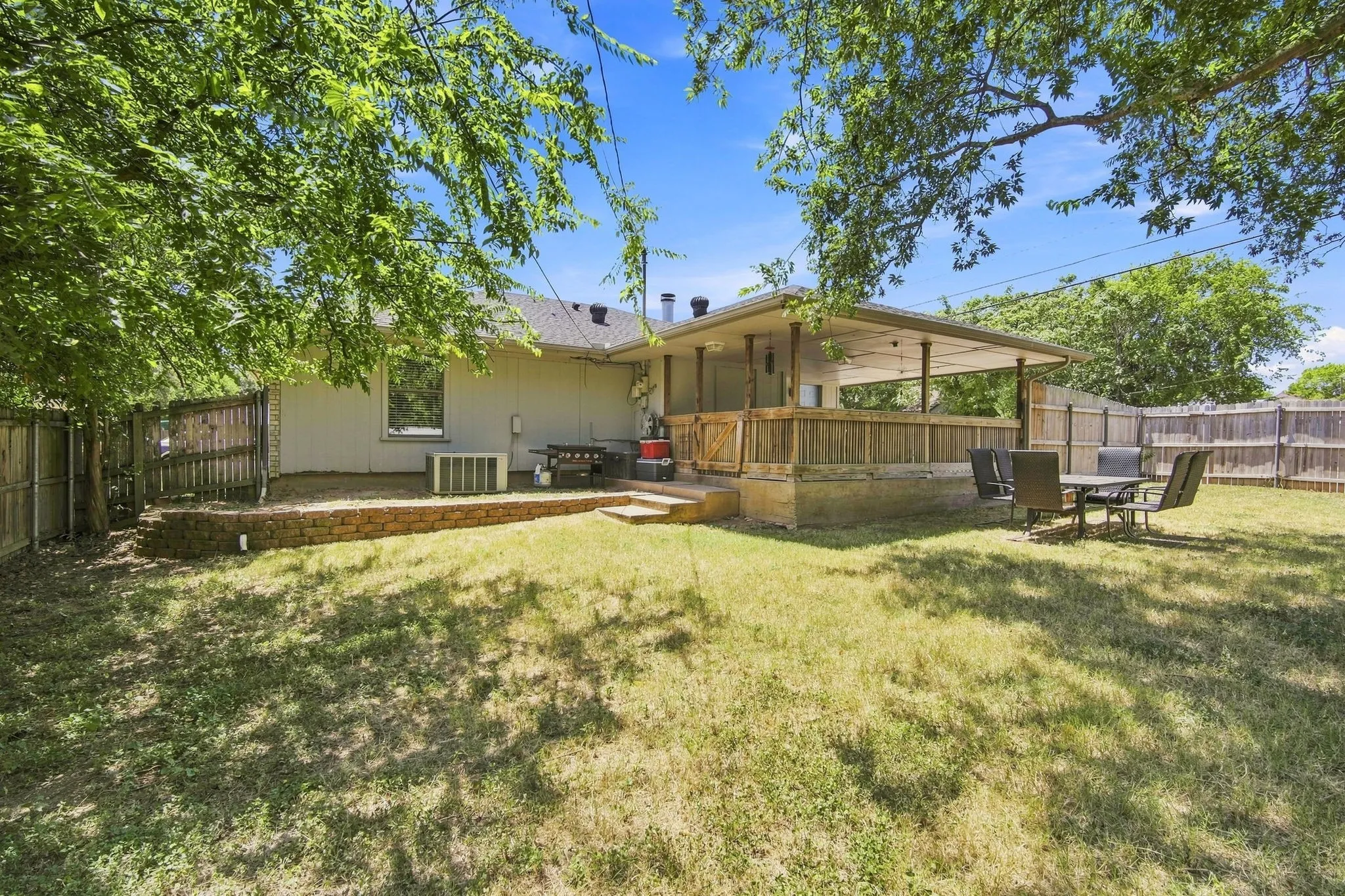 Rear exterior featuring a covered patio, wood privacy fence, and a spacious grassy backyard, perfect for outdoor living.