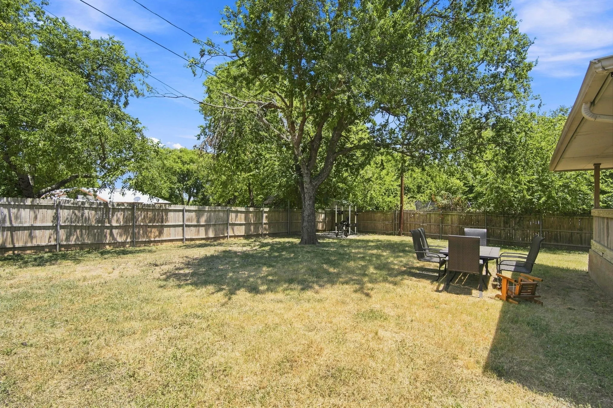 Expansive fenced backyard shaded by a mature tree, offering plenty of room to garden, play, or unwind.