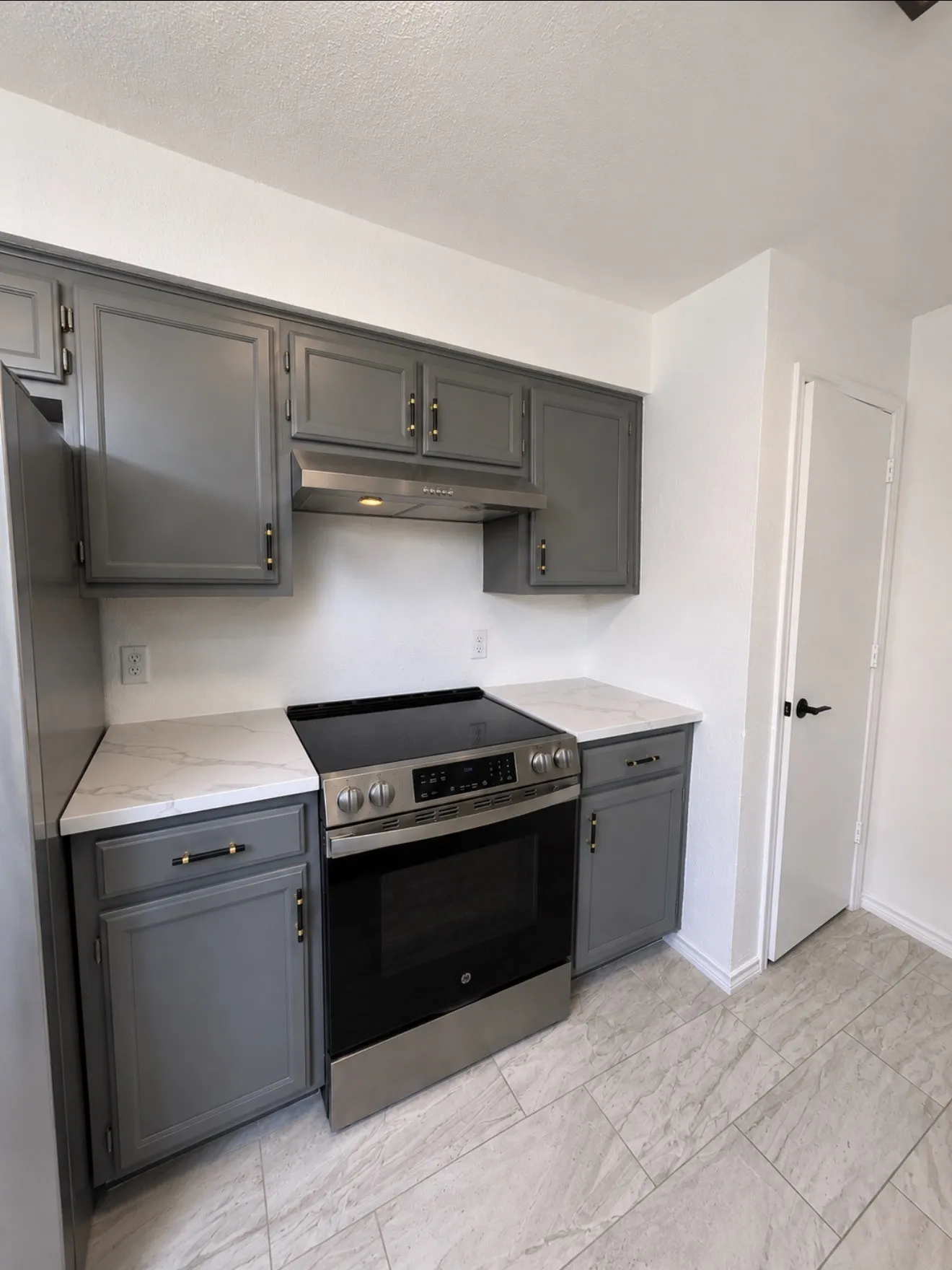 Modern kitchen featuring stainless steel appliances including a slide-in electric range and built-in microwave, gray cabinetry with hardware accents, white subway tile backsplash, and light wood-finish flooring