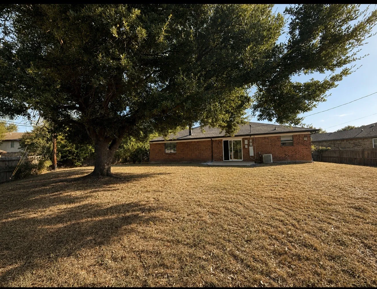 Brick ranch home situated on expansive grounds featuring a mature shade tree, open lawn, and single-story construction with direct outdoor access