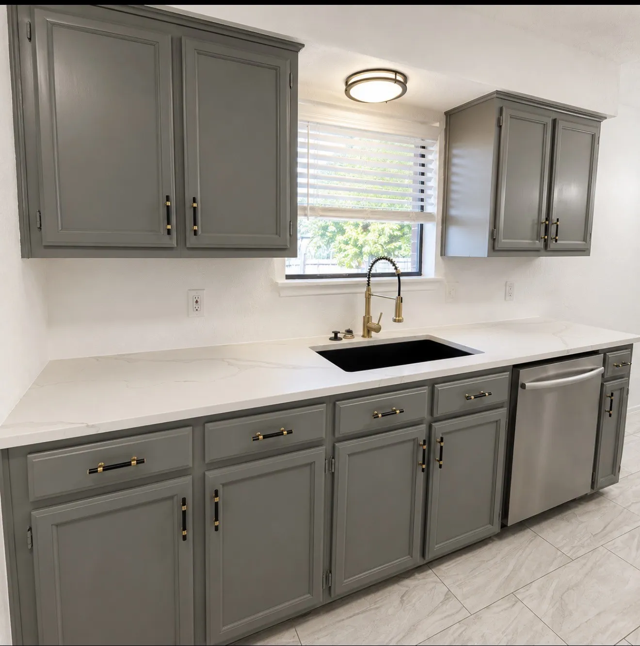 Kitchen featuring gray cabinetry with gold-tone hardware, white countertops, a black undermount sink with a gold-tone faucet, and a stainless steel dishwasher