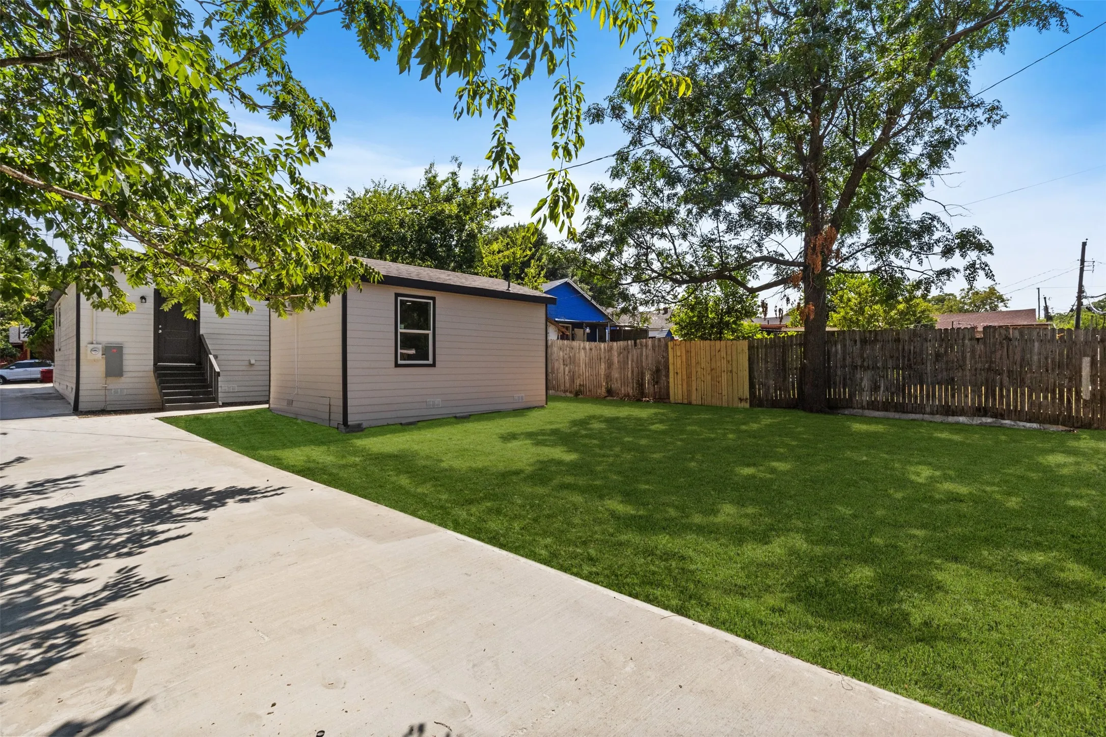 Spacious backyard featuring a manicured lawn, mature shade trees, and wooden privacy fencing