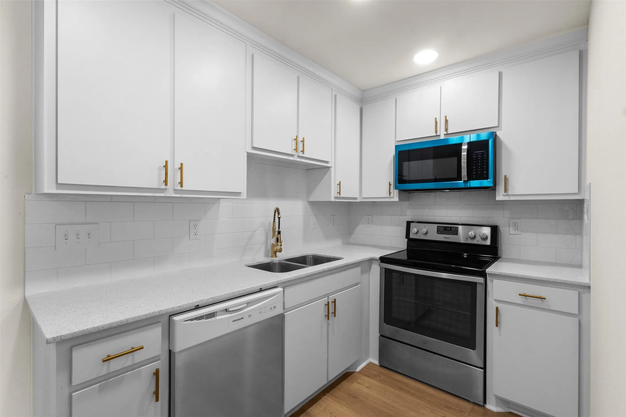 Modern kitchen featuring white cabinetry with gold-tone hardware, a subway tile backsplash, and light-toned countertops