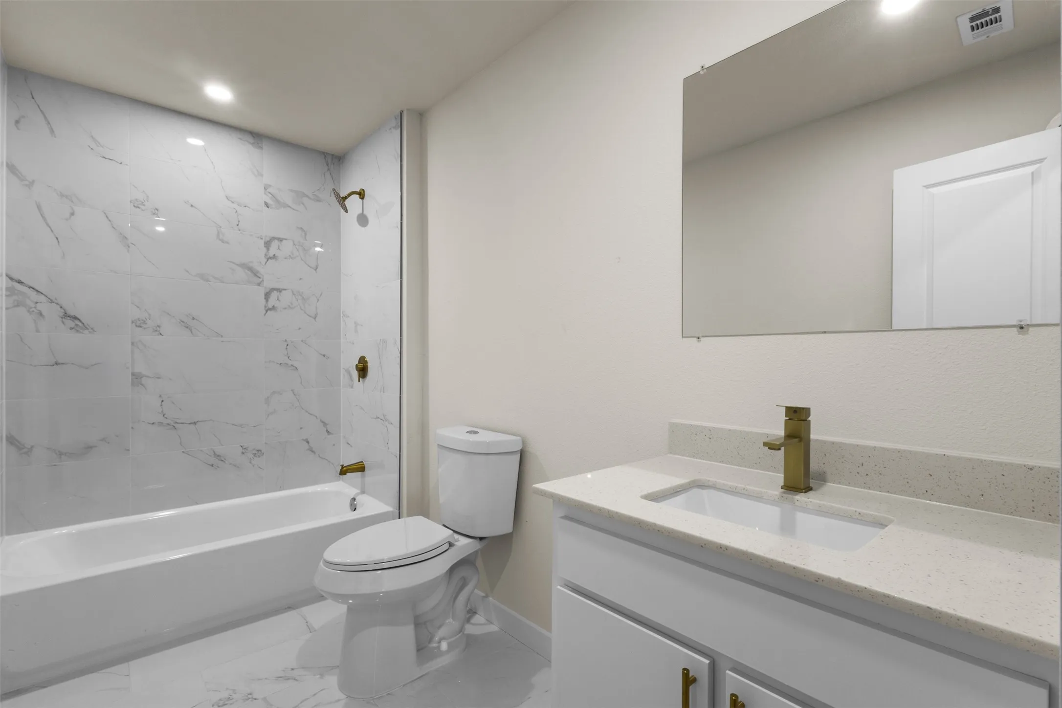 Modern bathroom featuring a marble-look tiled shower enclosure with frameless glass door, floating vanity with integrated sink and brushed brass faucet, quartz countertop, large illuminated mirror, and white ceramic tile flooring throughout