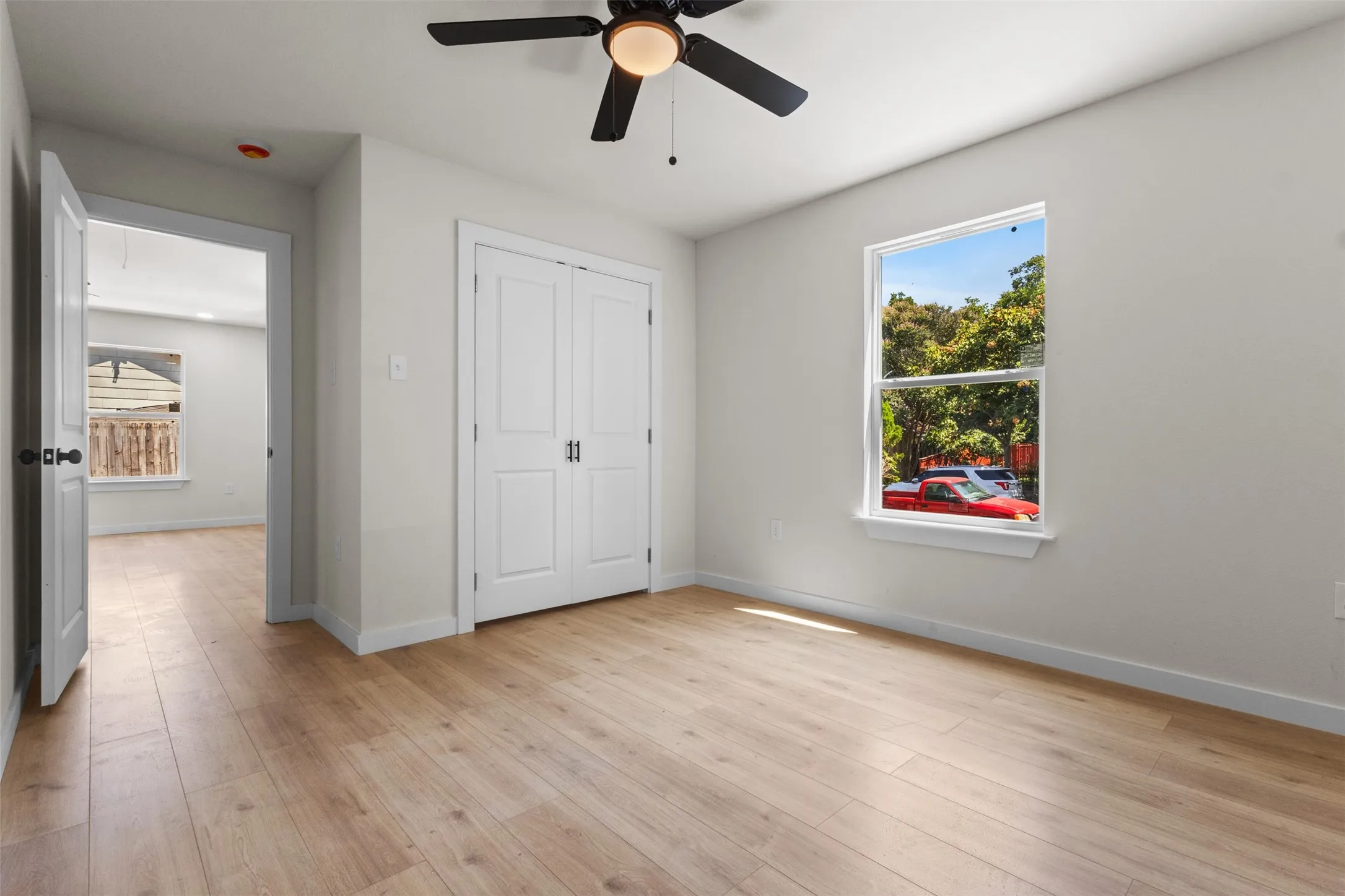Bright, light-filled bedroom featuring wood-finish flooring throughout, a ceiling fan with integrated lighting, and a large window with natural light