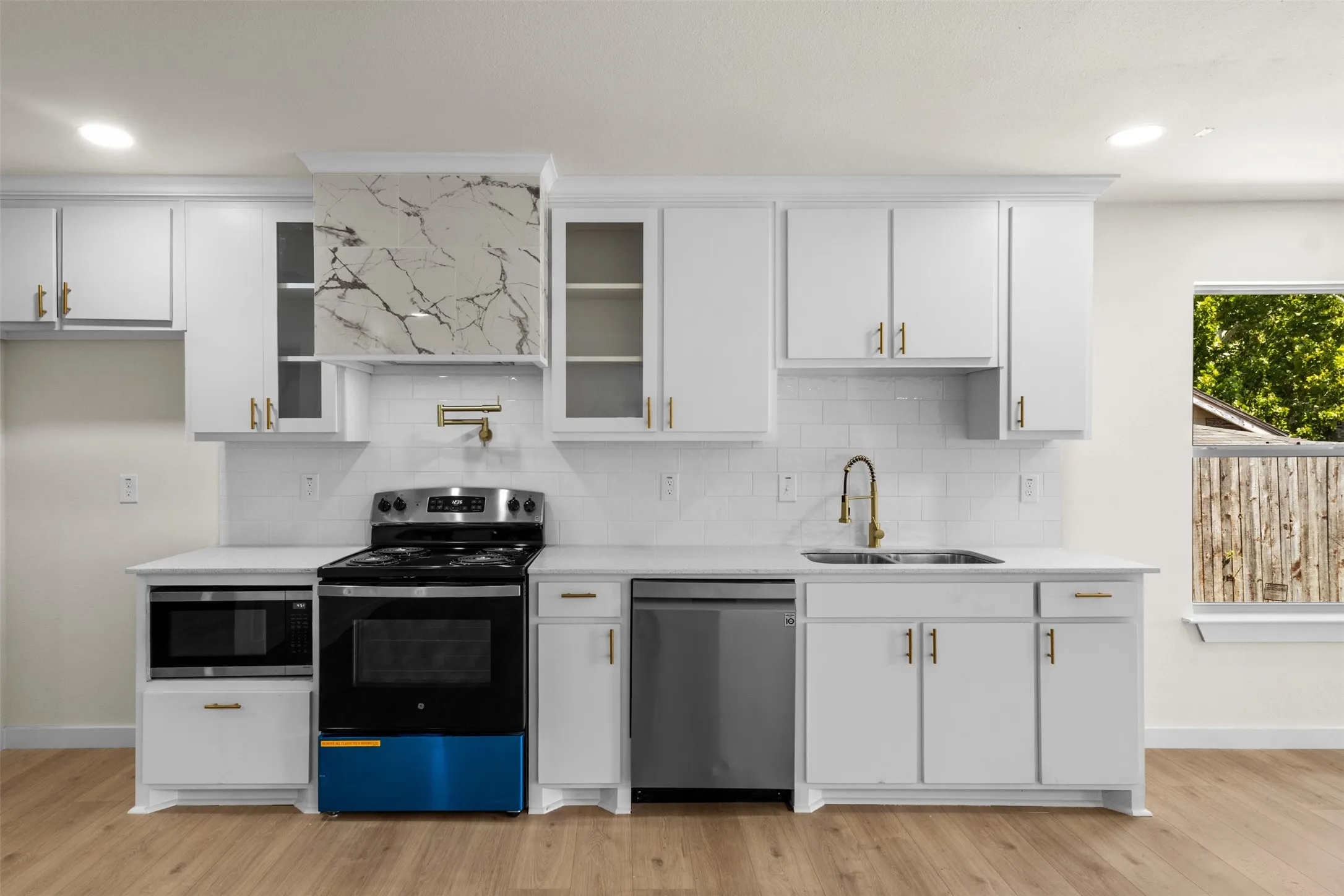 Modern kitchen featuring white shaker-style cabinetry with brushed nickel hardware, quartz countertops with marble-look veining, and a coordinating tile backsplash