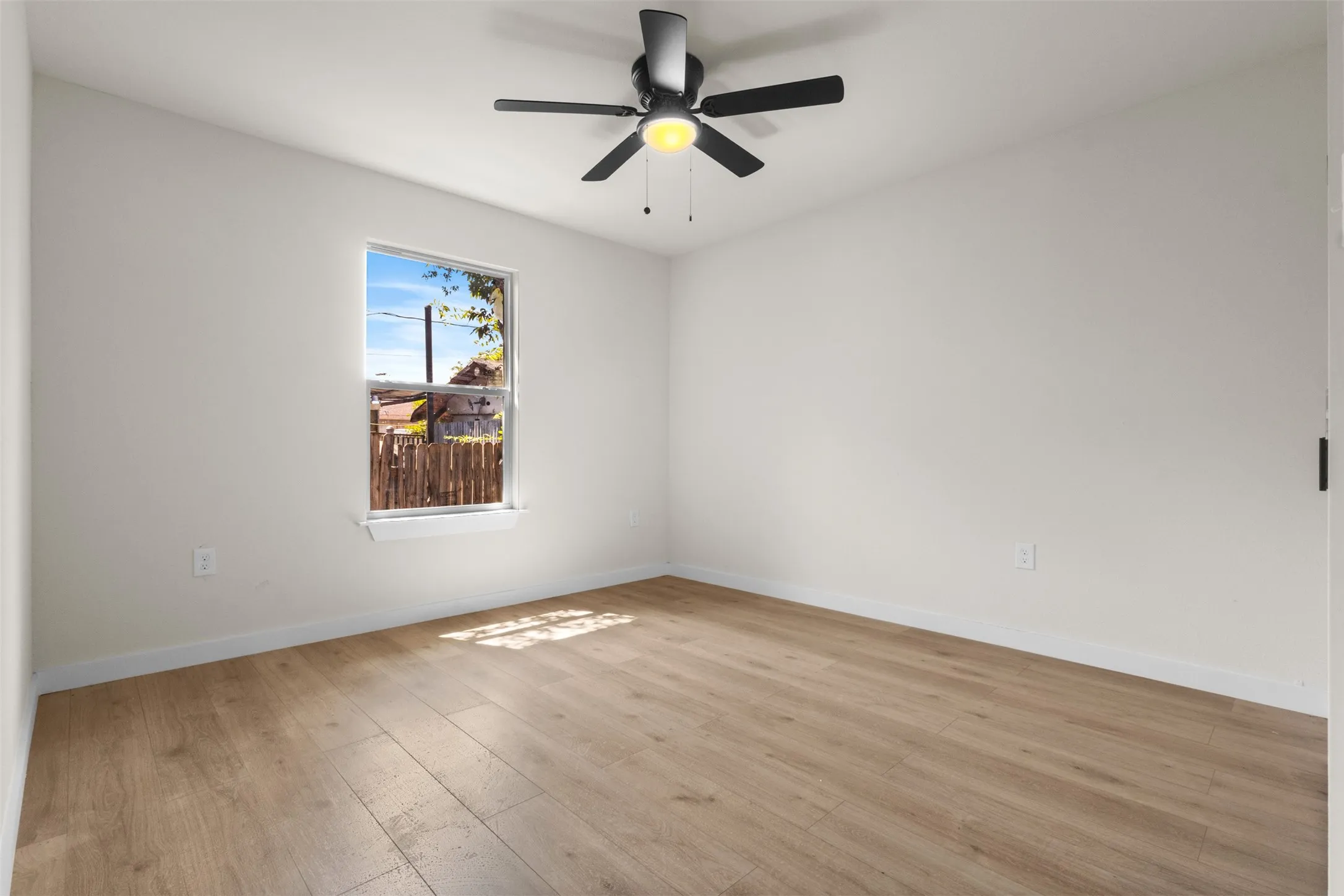 Spacious room with wood-finish flooring, white walls, and a ceiling fan with integrated lighting