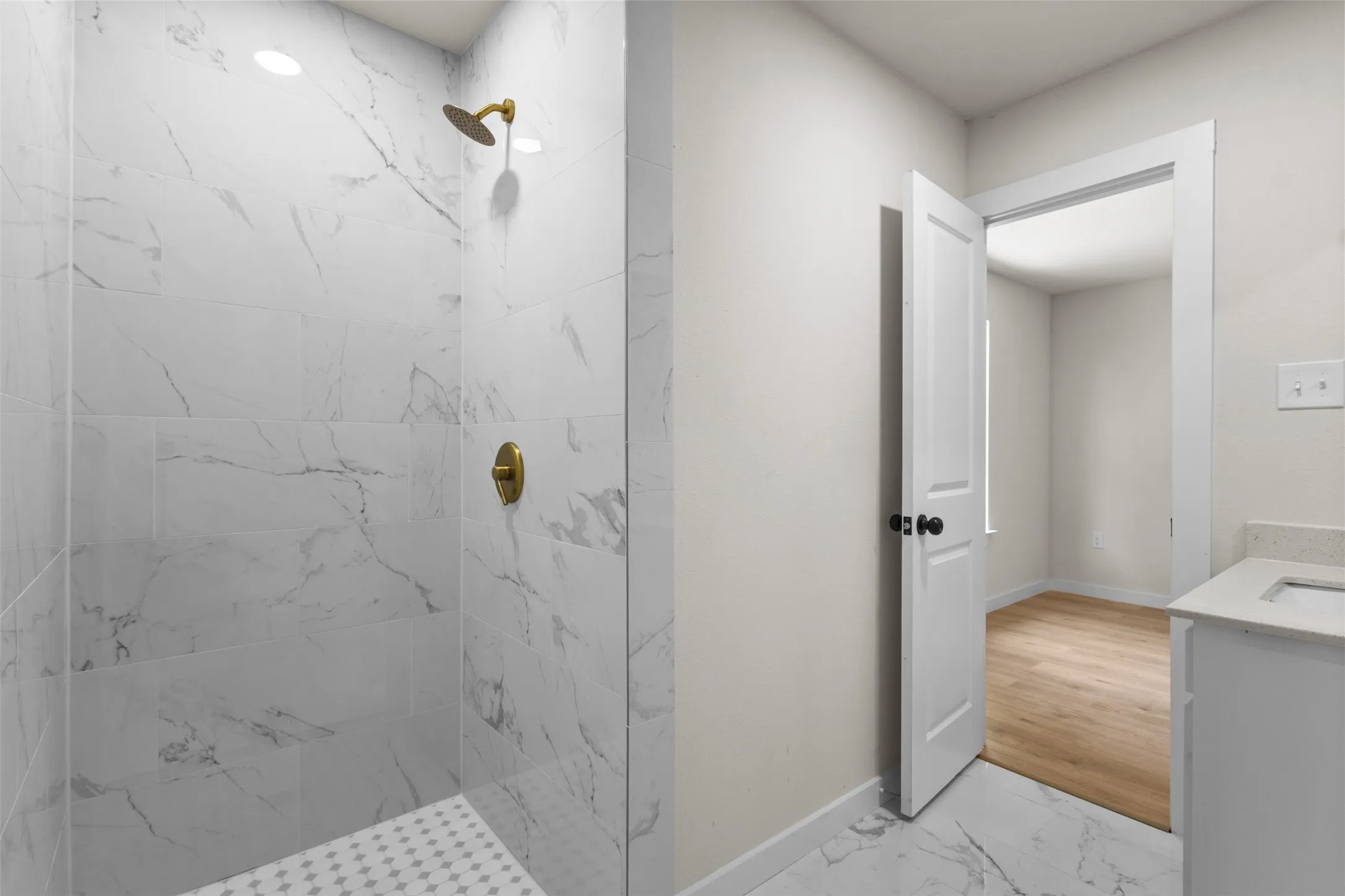 Shower with gold-toned fixtures, white marble-patterned tile, and a white mosaic tile floor