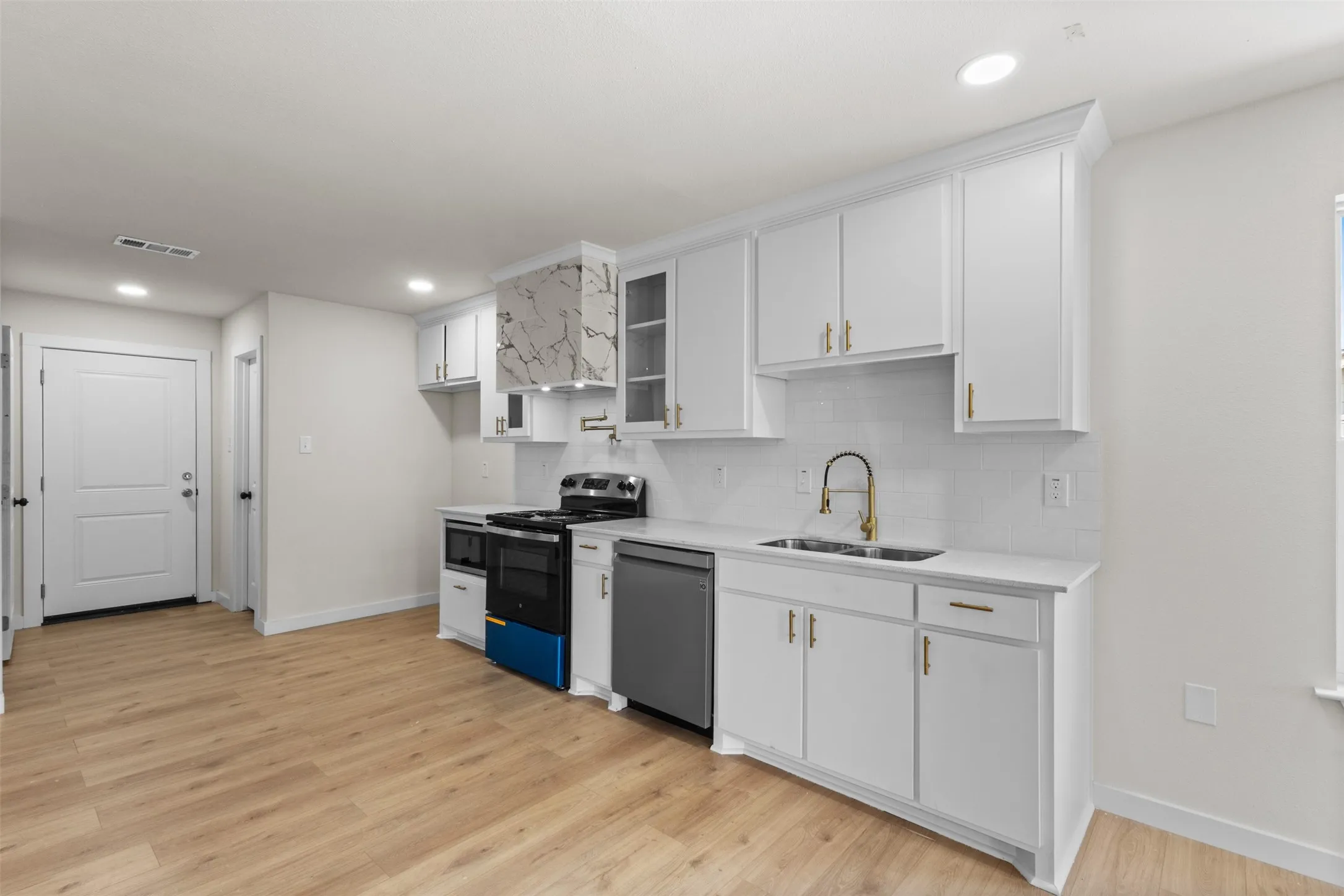 Modern kitchen featuring white shaker-style cabinetry with brushed nickel hardware, quartz countertops, and stainless steel appliances including a gas range and dishwasher