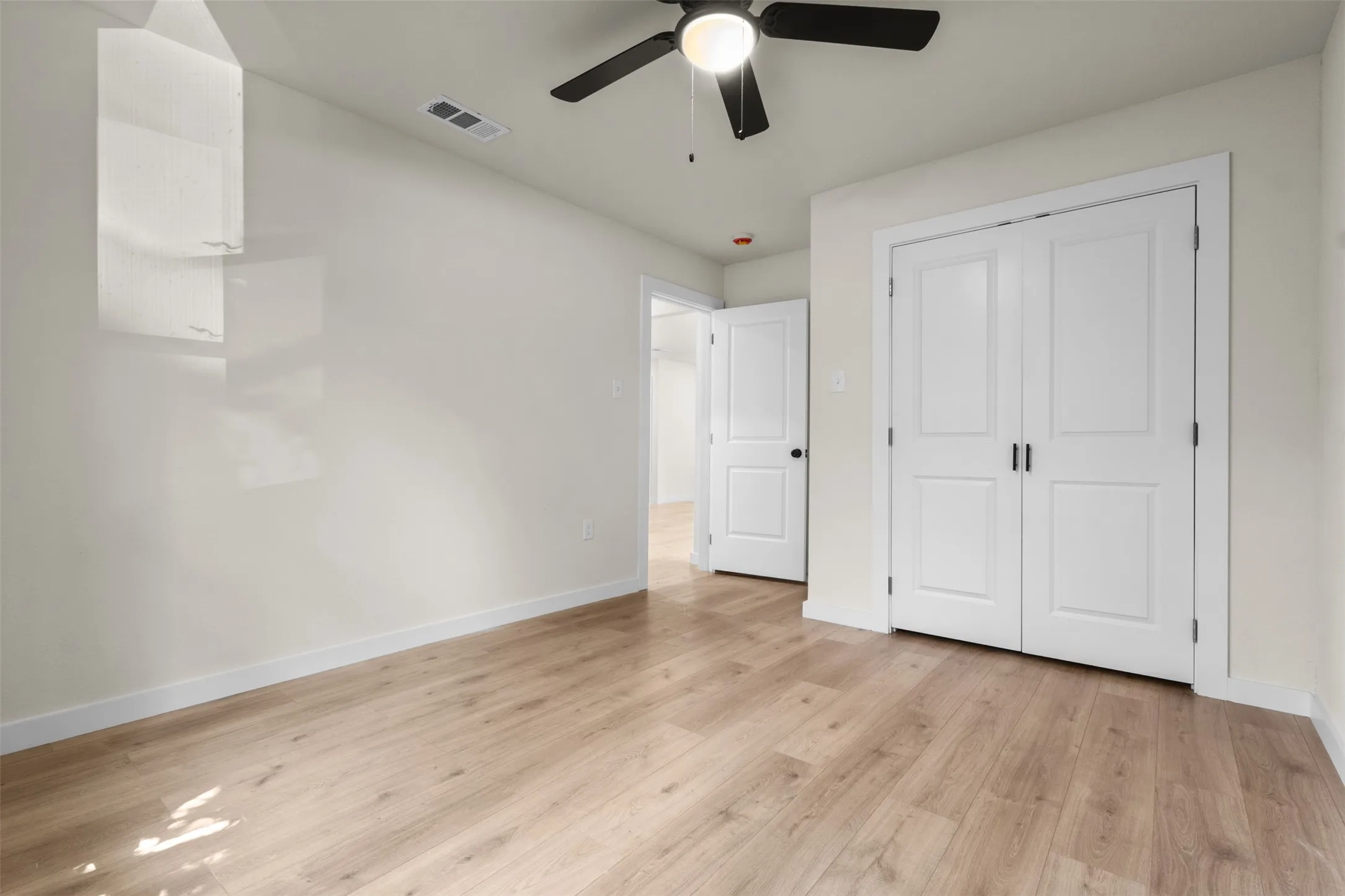 Spacious bedroom showcasing pristine white 6-panel closet doors, light wood-finish flooring, and neutral walls with excellent natural lighting